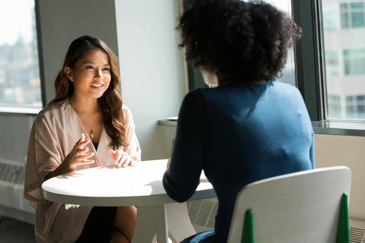 A mentor and mentee in conversation across a table in a bright office